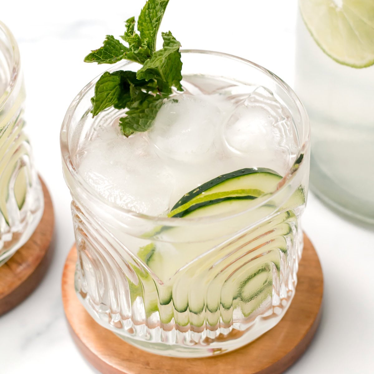 A glass of iced cucumber water with mint garnish rests on a wooden coaster, perfect for refreshing sips as you browse our Recipe Index.