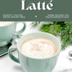 Mint green mug of eggnog latte topped with nutmeg, with greenery and ornaments in the background.