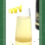 A champagne glass with a pale yellow elderflower French 75 cocktail and a lemon twist garnish.