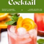 A pink cocktail with ice, orange peel, and mint garnish in a glass on a wooden coaster.