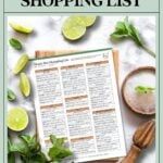 Home bar shopping list on a clipboard, surrounded by mint, limes, a wooden juicer, and a cocktail glass.