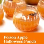 Round glasses of orange apple punch with star anise, set on a table for Halloween, with green apples behind.