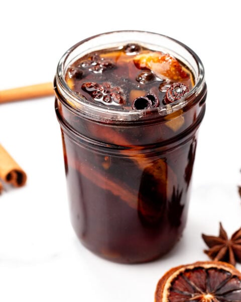 A glass jar filled with iced spiced drink, garnished with dried orange slices and star anise.