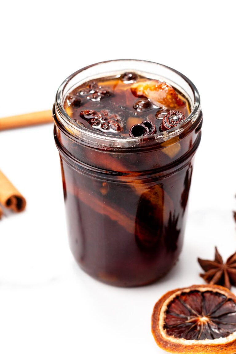 A glass jar filled with iced spiced drink, garnished with dried orange slices and star anise.