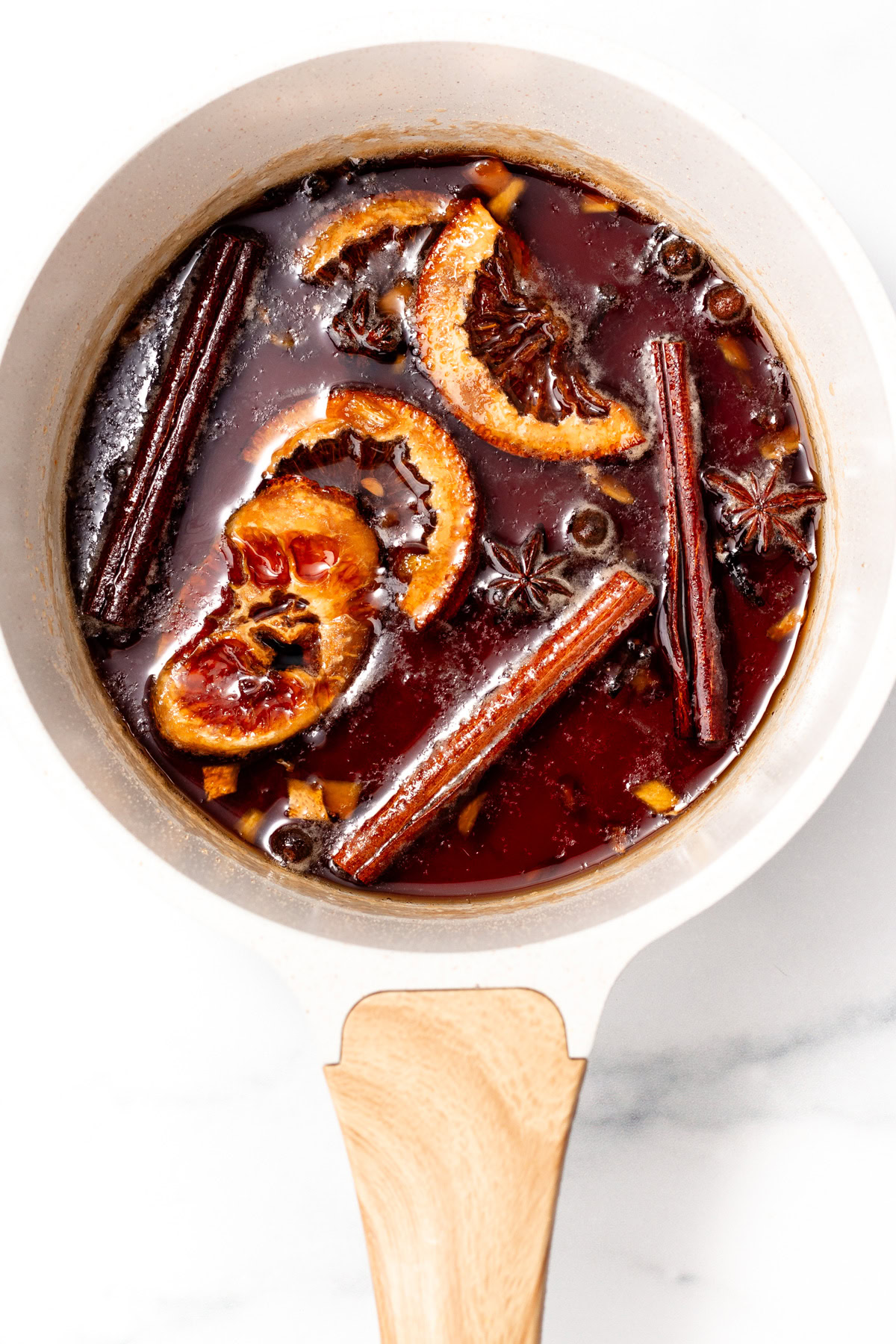 A pot of mulled wine with orange slices, cinnamon sticks, star anise, and spices on a white background.