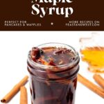 A jar of spiced maple syrup with cinnamon sticks and star anise, surrounded by more spices and maple syrup.