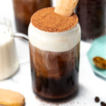 Iced coffee topped with whipped cream, cocoa powder, and a ladyfinger cookie in a glass jar.