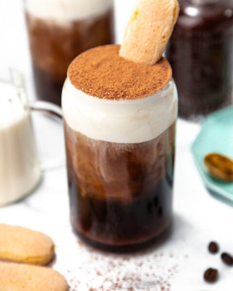 Iced coffee topped with whipped cream, cocoa powder, and a ladyfinger cookie in a glass jar.