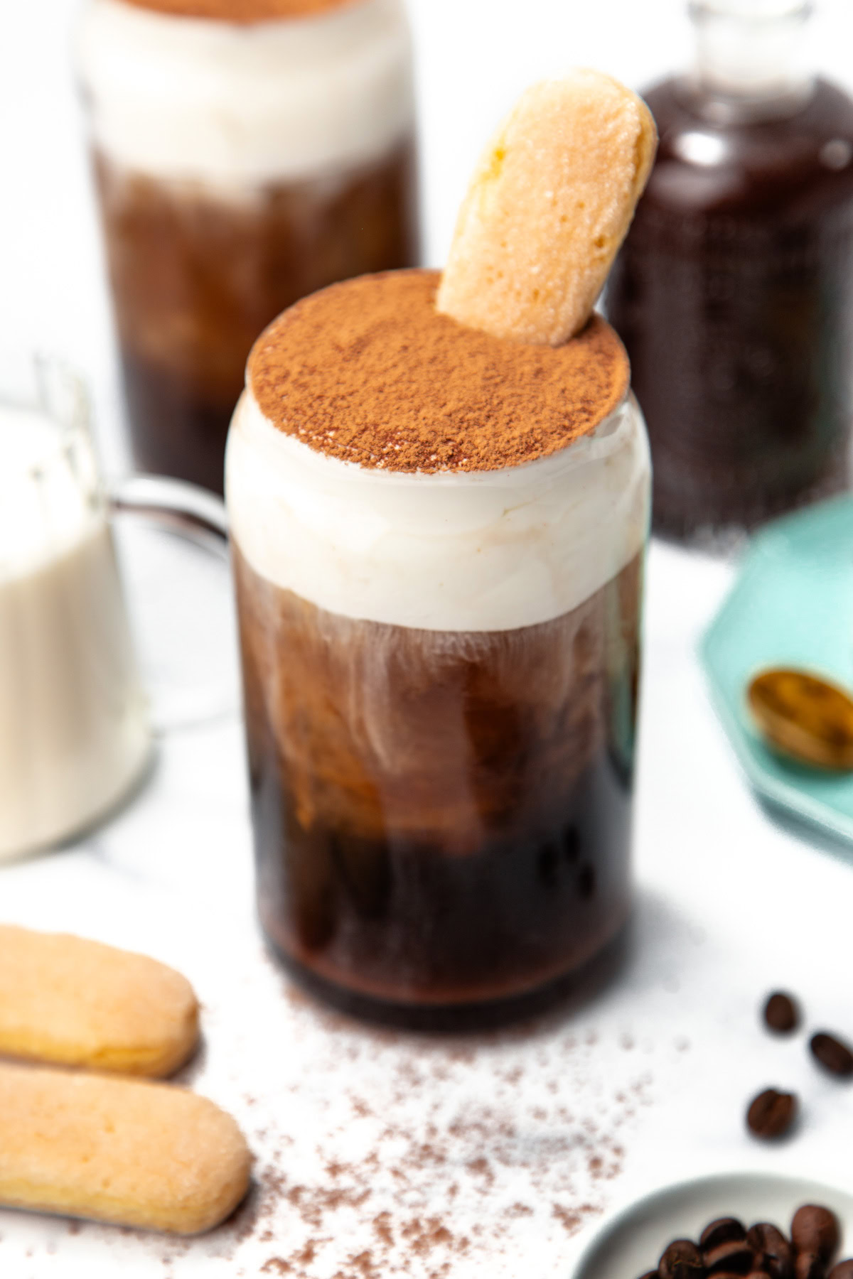 Iced coffee topped with whipped cream, cocoa powder, and a ladyfinger cookie in a glass jar.