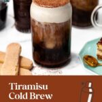 A glass of tiramisu cold brew topped with foam, a ladyfinger, and cocoa, with tiramisu and ladyfingers nearby.