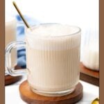 A mug of frothy babyccino on a wooden coaster with a gold spoon.