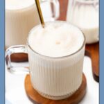 A kid-friendly cappuccino in a ribbed glass mug with a spoon.