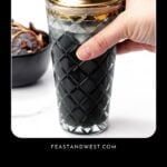 A hand holding a glass cocktail shaker filled with a black drink, with text reading “Black-colored cocktails for parties.”