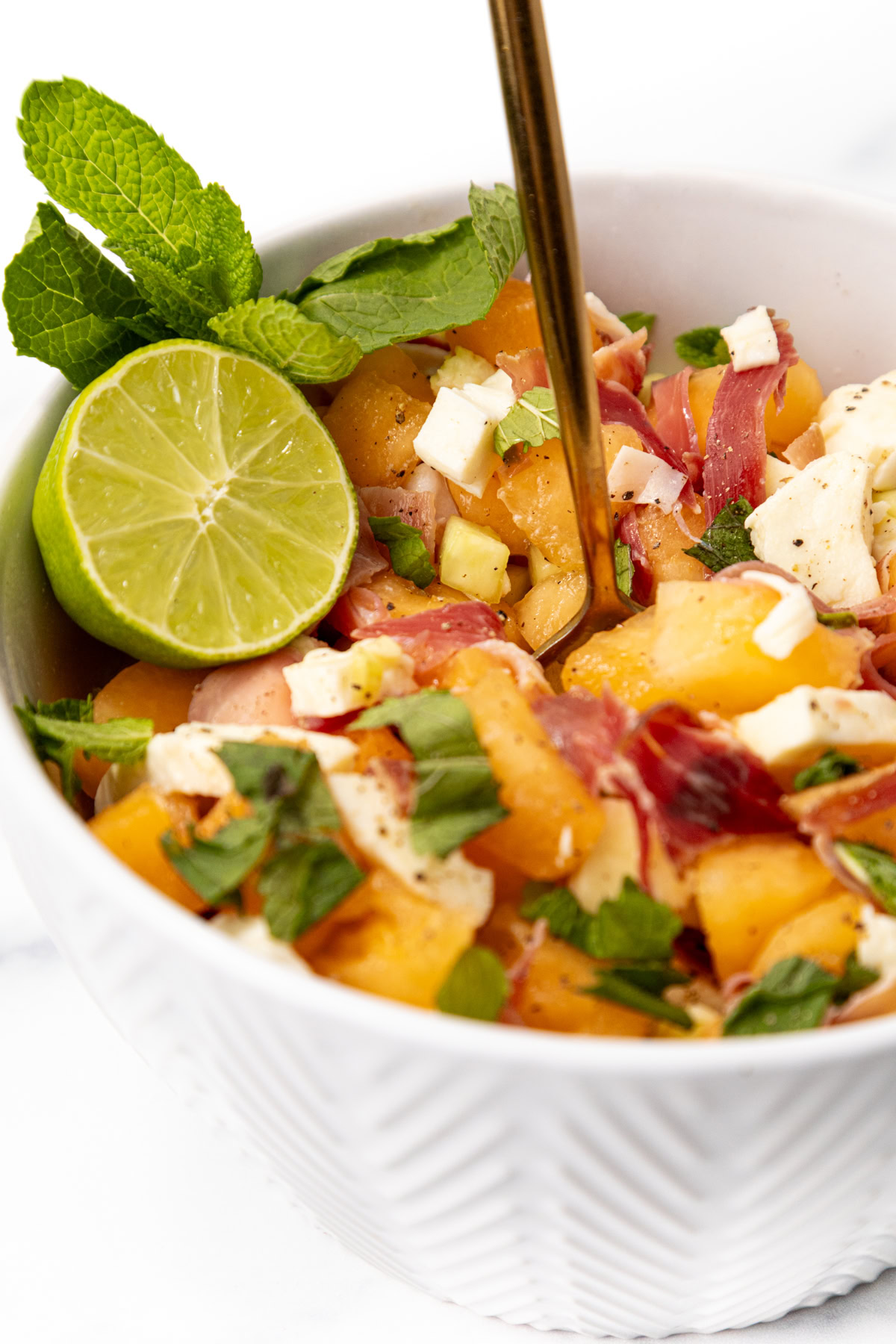 Cantaloupe, prosciutto, and feta salad in a bowl, garnished with a lime slice and fresh mint.