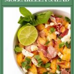 Cantaloupe and mozzarella salad with prosciutto, mint, and a lime slice in a white bowl.