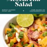 A bowl of melon, prosciutto, and mozzarella salad garnished with mint and a lime slice.