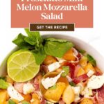 A salad of melon, prosciutto, and mozzarella topped with mint and lime in a white bowl.