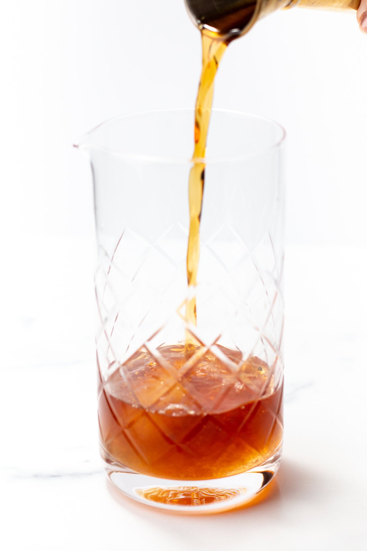 Amber liquid being poured into a cut-glass mixing glass with ice.