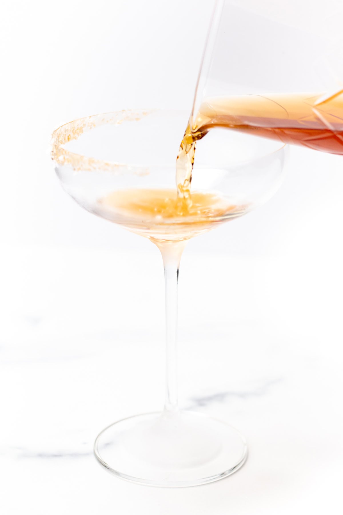 Amber liquid being poured into a rimmed coupe glass.