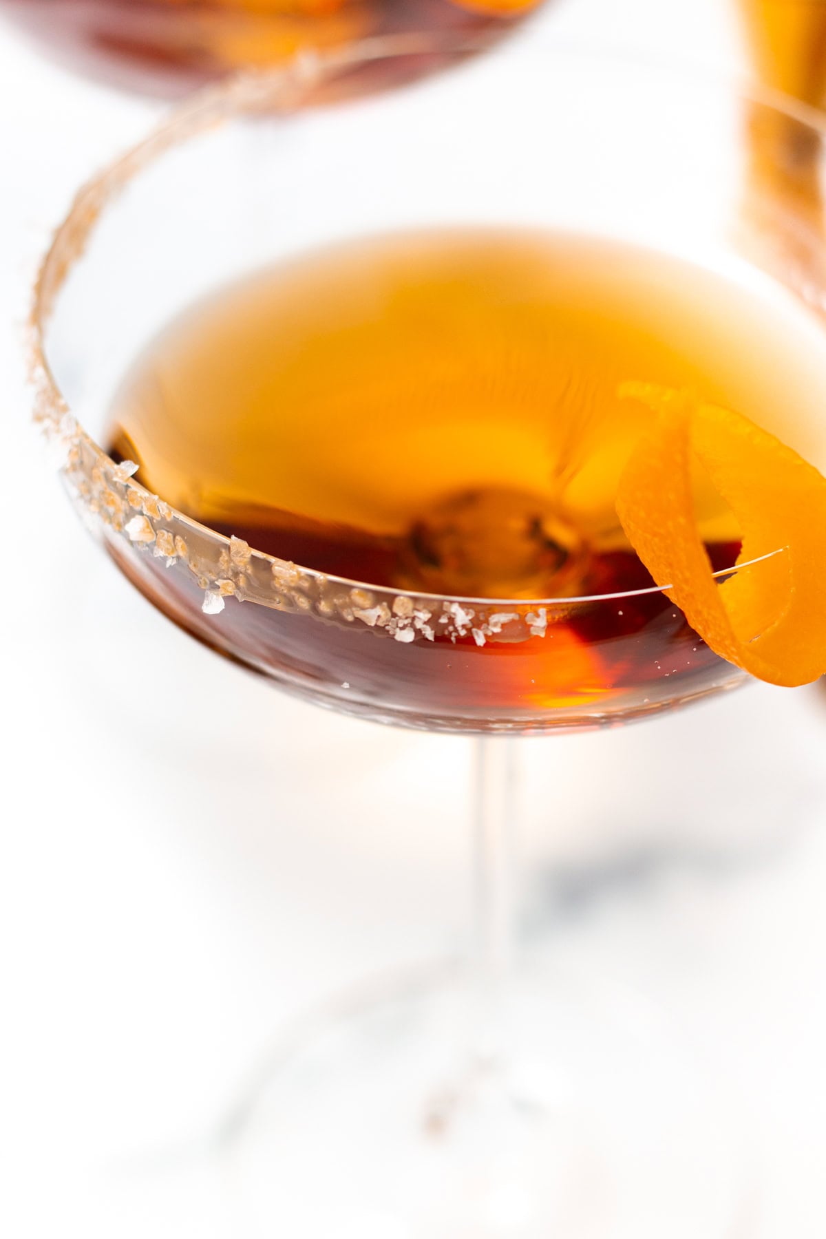 Amber cocktail in a stemmed glass with a salt-rimmed edge and an orange peel twist.