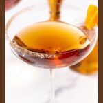 Salted caramel Manhattan cocktail in a coupe glass with a salt rim and orange peel garnish.