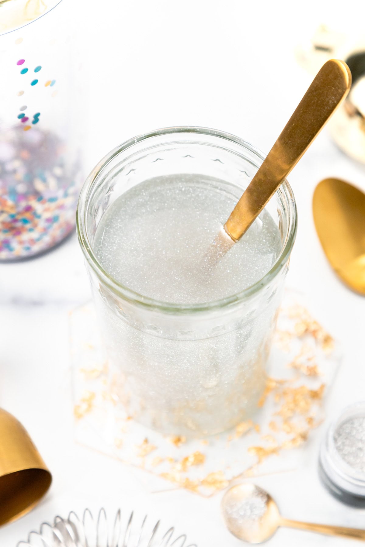 Glass of clear, shimmery liquid with a gold spoon.