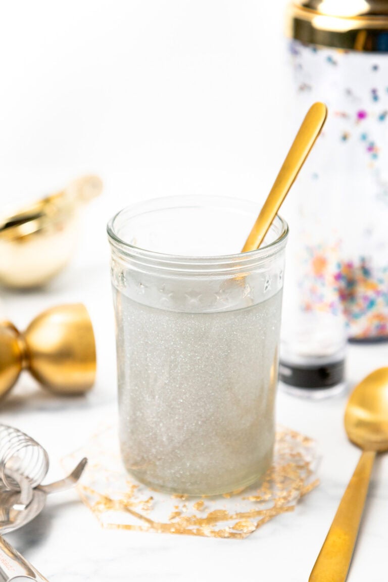 A glass of shimmering silver cocktail with a gold spoon, surrounded by bar tools.