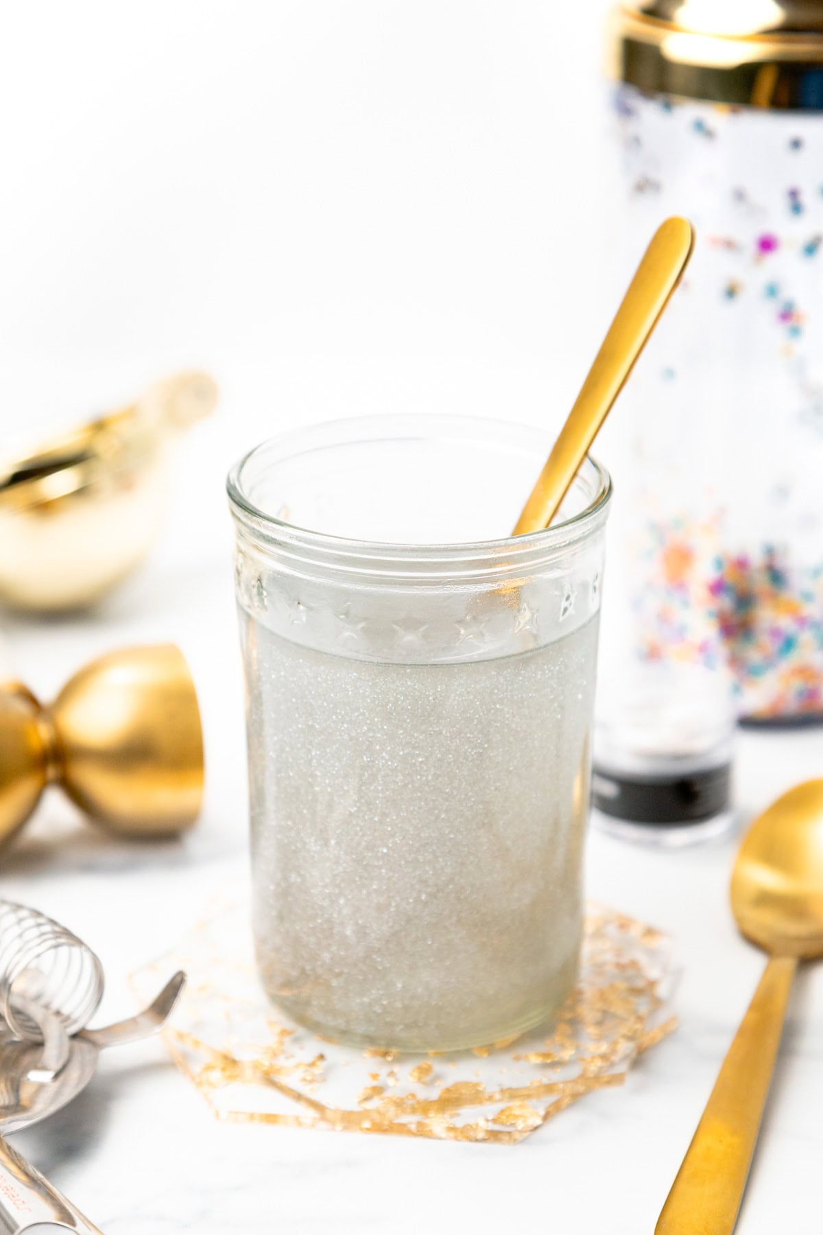 A glass of shimmering silver cocktail with a gold spoon, surrounded by bar tools.