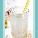 A glass of shimmering, edible glitter syrup with a gold straw, next to a jar of silver luster dust.