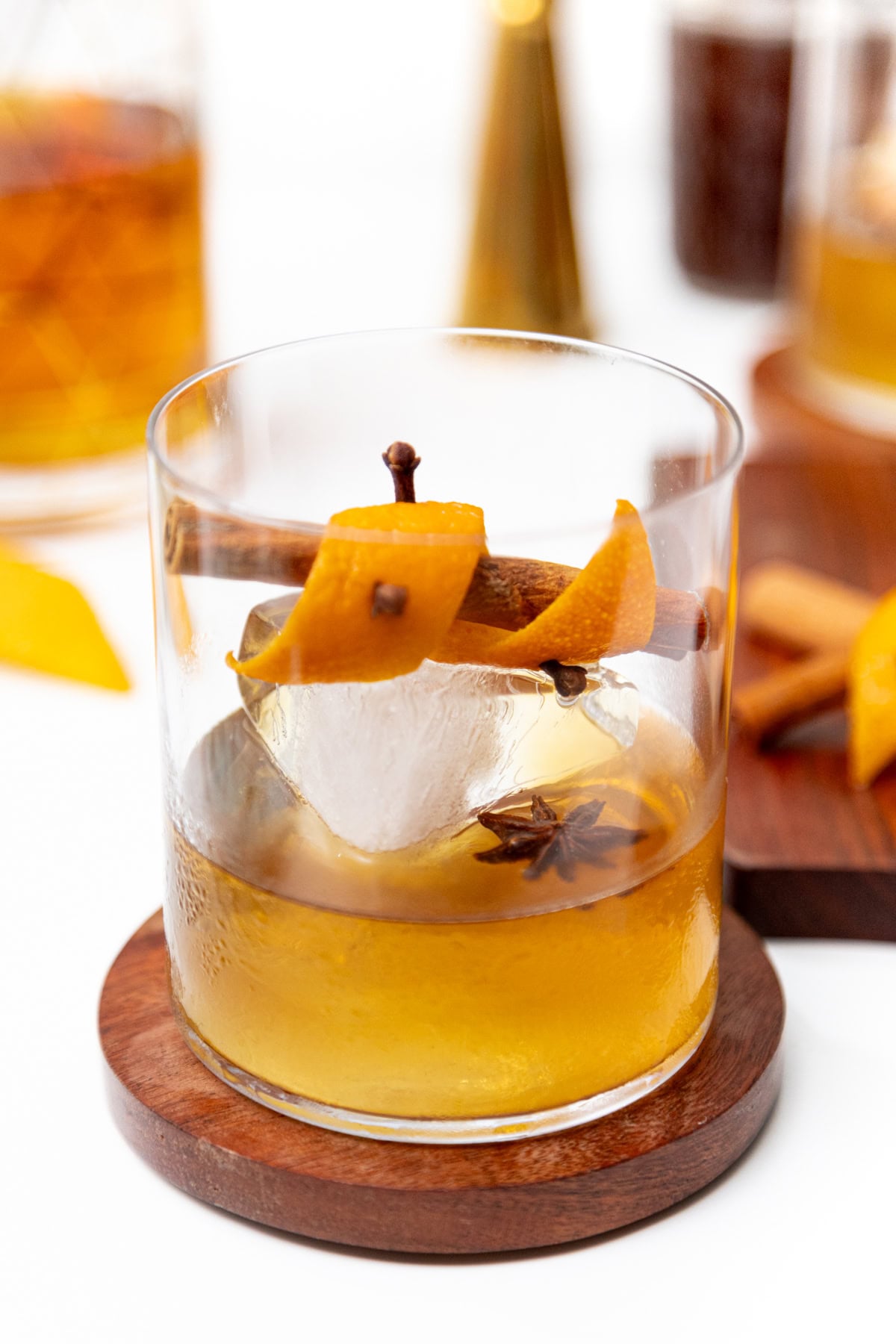 An old fashioned cocktail garnished with an orange twist, cinnamon stick, cloves, and star anise over a large ice cube.