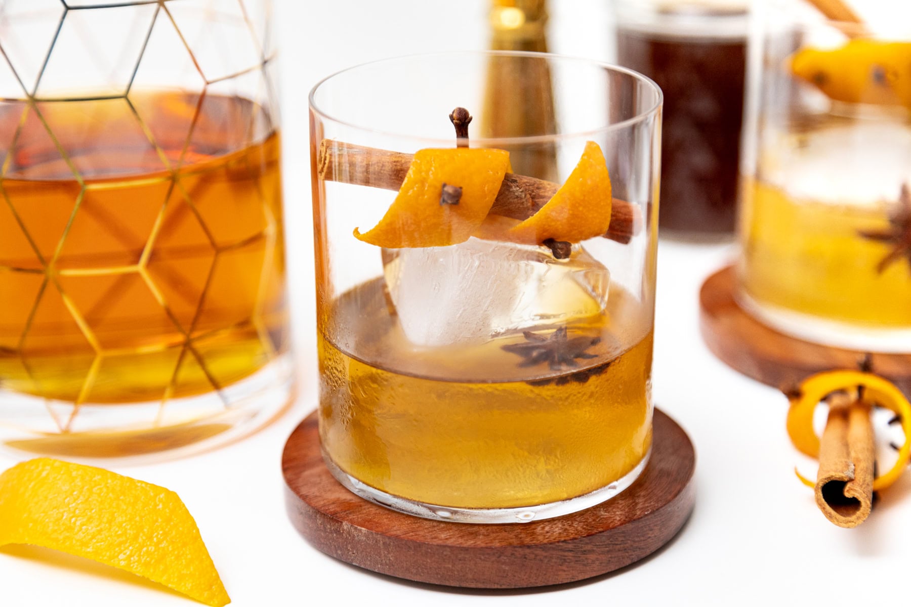 An old fashioned cocktail garnished with a cinnamon stick, orange peel, cloves, and a star anise.